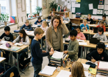 Teacher assisting students with papers while classmates work at desks